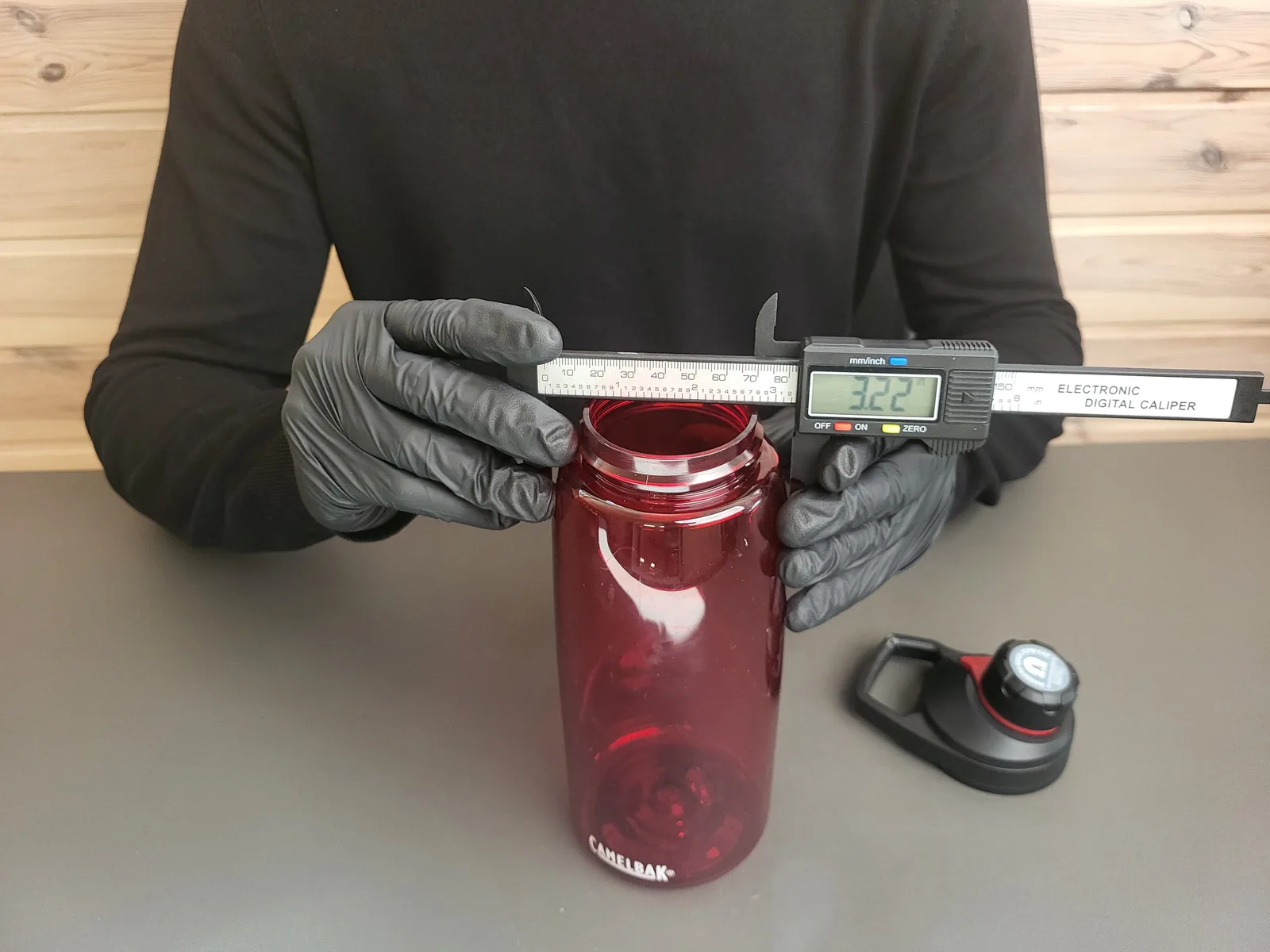 A digital caliper measuring the opening of a red reusable bottle.