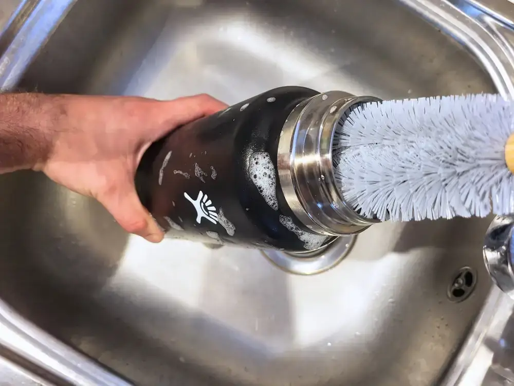 Hand-cleaning a bottle with a bottle brush in a sink