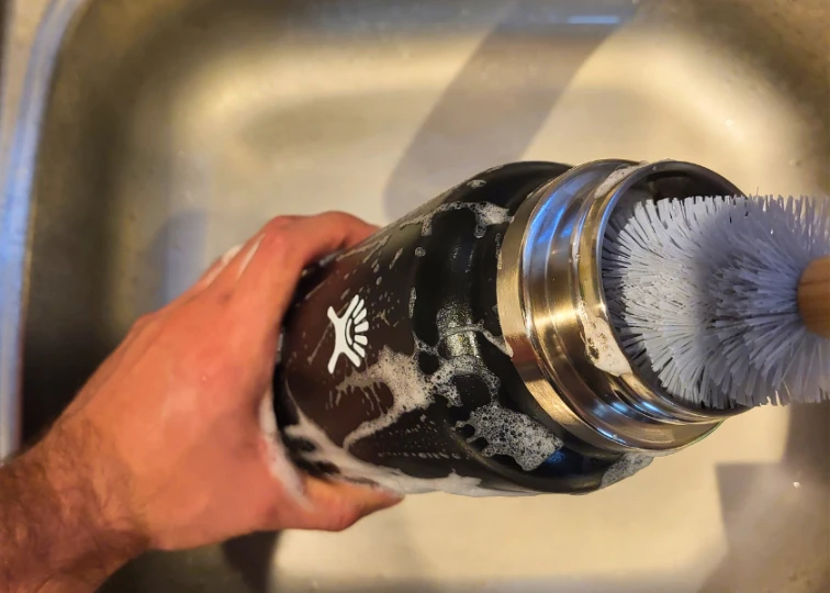 A black Hydro Flask water bottle being cleaned with a brush in a sink.