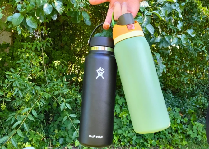 A man holding a black Hydro Flask and a green Owala FreeSip by the handles.