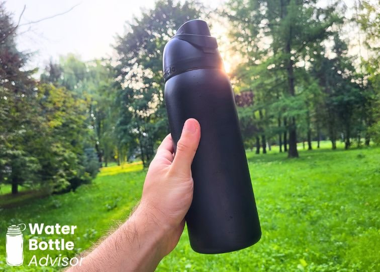 Owala FreeSip 32 oz black bottle being held outdoors in a grassy park
