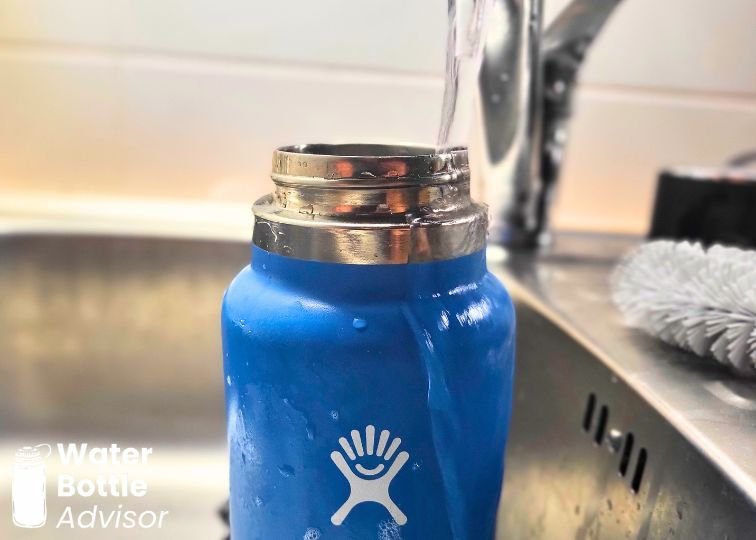 Hydro Flask 32 oz bottle being rinsed with water in a kitchen sink