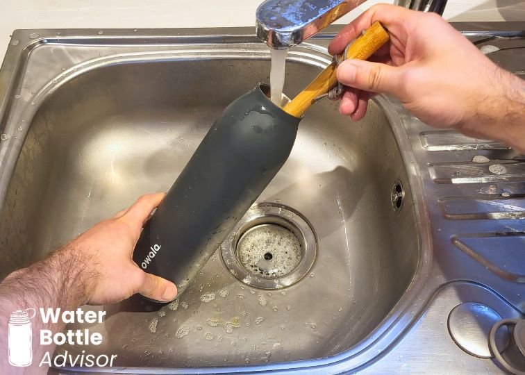 Owala FreeSip Twist 24 oz bottle being cleaned with a brush under running water in a sink
