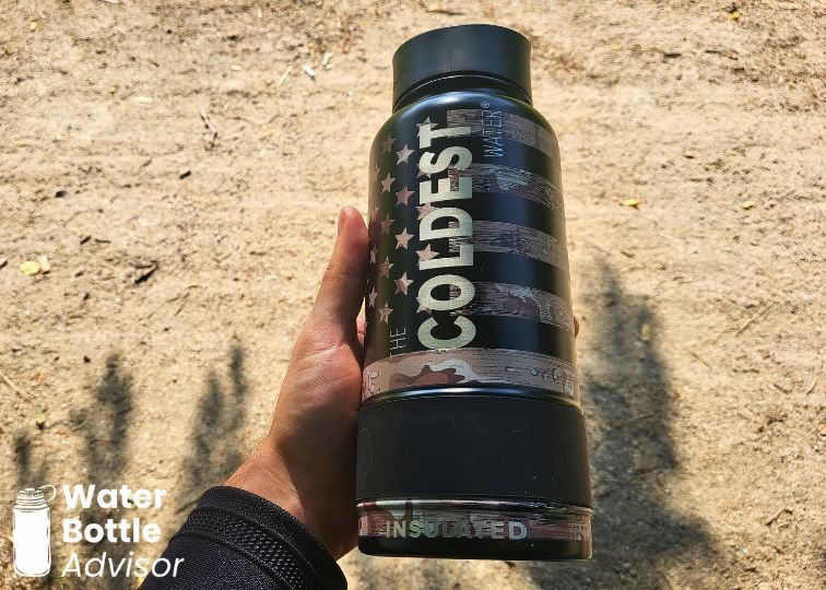 Close-up of the Coldest 32 oz black water bottle with flag-style design being held outdoors