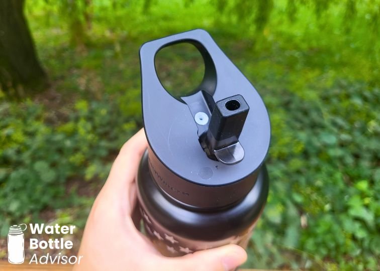 Close-up of the Coldest 32 oz black water bottle straw lid with carry handle held outdoors