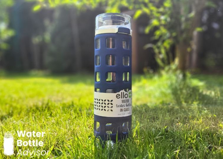 Ello Syndicate glass water bottle with blue silicone sleeve standing outdoors in the grass