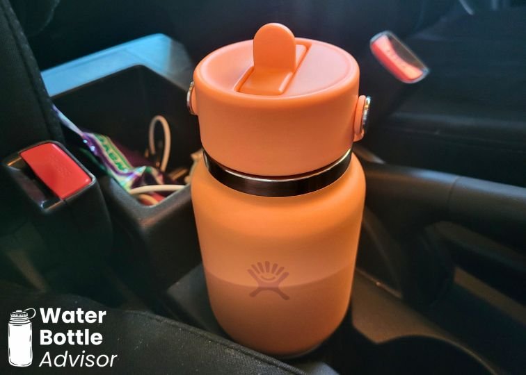 Hydro Flask 24 oz orange travel bottle sitting in a car cup holder