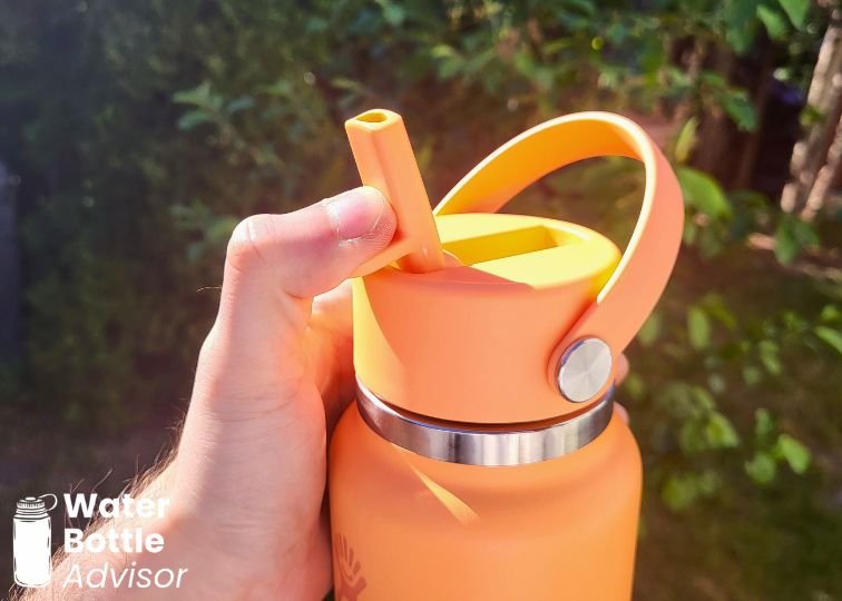 Close-up of the Hydro Flask 24 oz orange travel bottle showing the straw lid and carry handle outdoors