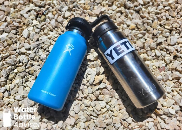 Hydro Flask 32 oz bottle and YETI Rambler 26 oz bottle lying on gravel outdoors