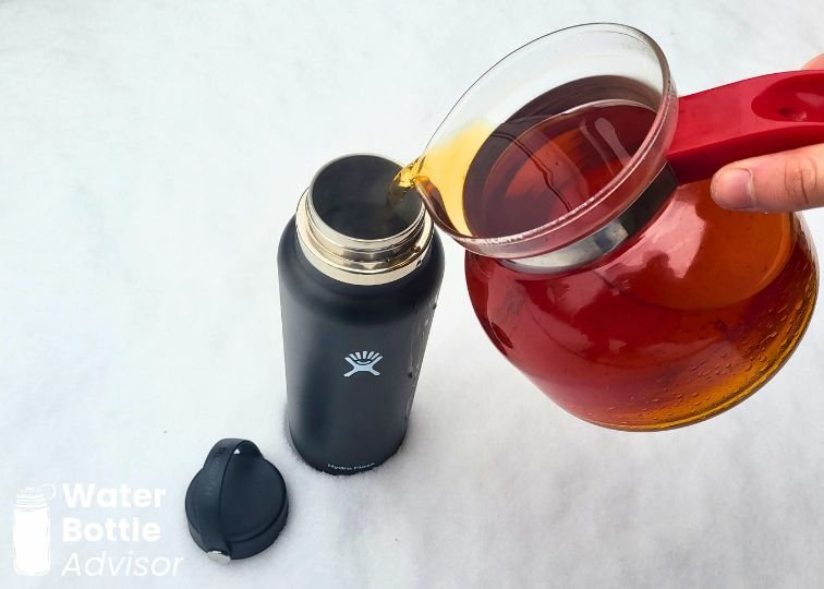 Hot tea being poured from a glass teapot into a Hydro Flask 40 oz bottle