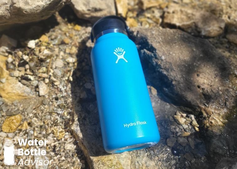 Hydro Flask Wide Mouth 32 oz blue water bottle lying on rocks in a shallow creek