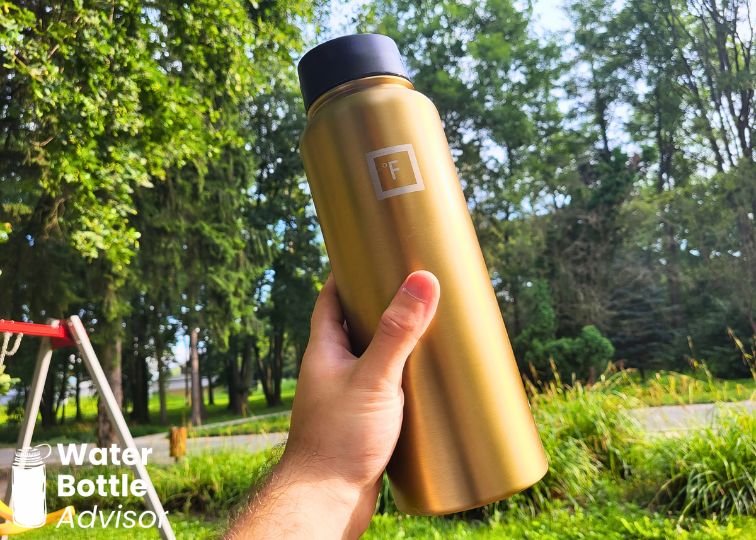 Iron Flask 40 oz gold bottle being held outdoors in a park