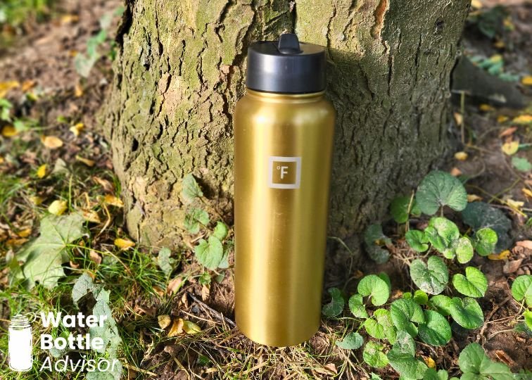 Iron Flask 40 oz gold bottle standing outdoors against a tree