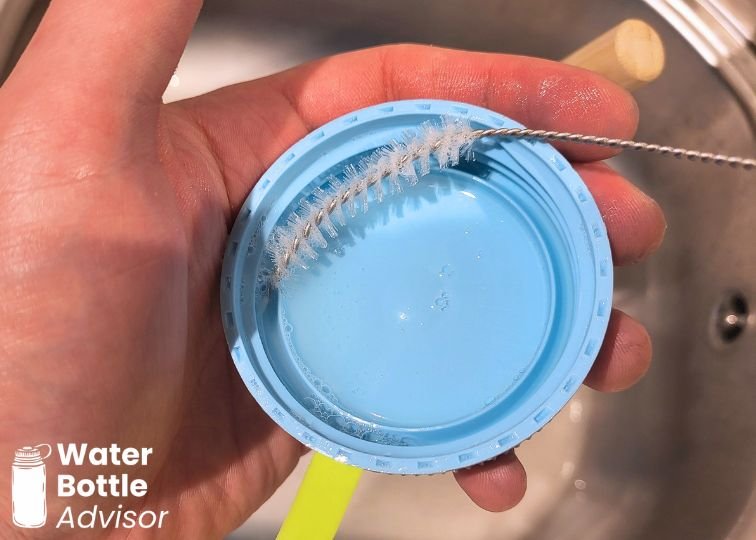 Nalgene wide mouth lid being cleaned with a straw brush under running water