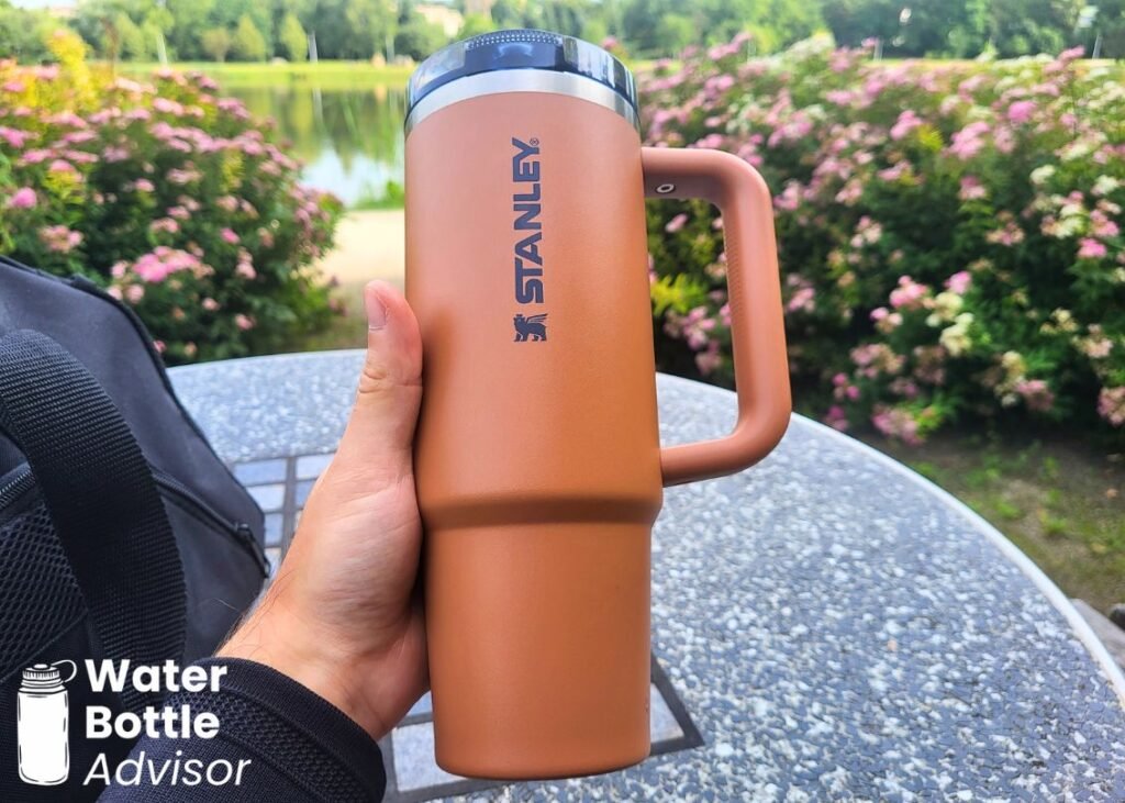 Stanley ProTour Tumbler 30 oz being held outdoors near flowers and a pond