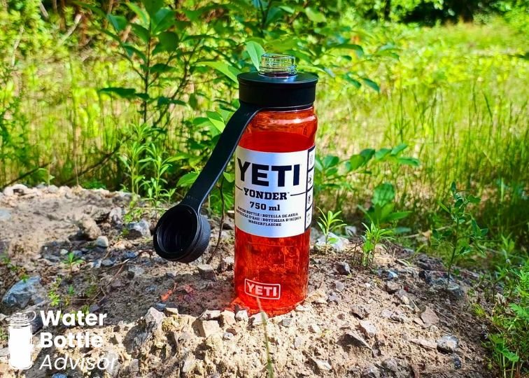 YETI Yonder 25 oz red plastic water bottle standing outdoors on rocks with greenery in the background