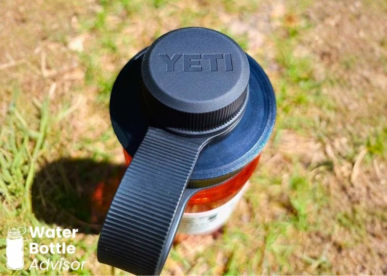 Close-up of the YETI Yonder 25 oz red plastic water bottle showing the black Tether Cap outdoors